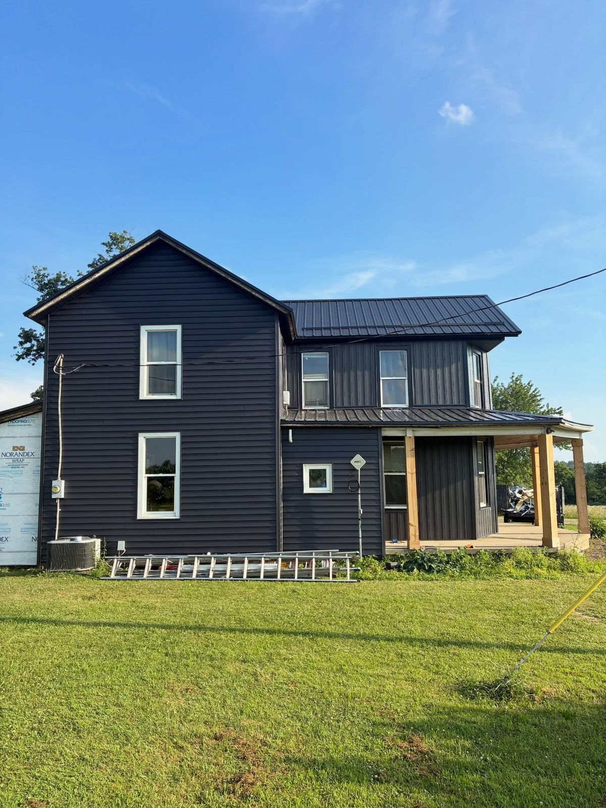 Same farmhouse after with dark lap siding, board and batten upper and a black metal roof