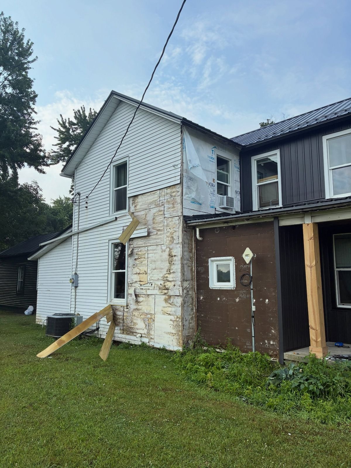 Farmhouse before the job with old white siding partly torn off and stained sheathing showing