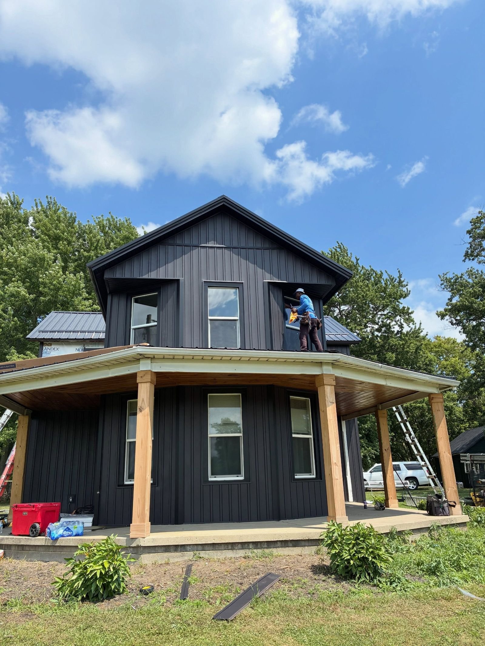 One Pro Exterior crew installing black board and batten siding on a farmhouse with a wraparound porch