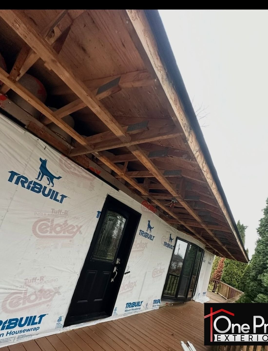 Wall wrapped in housewrap with a new black entry door, mid project